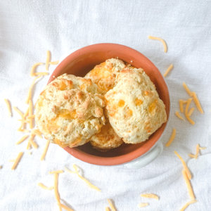 Top view of garlic cheddar biscuits in a crock surrounded by shredded cheddar