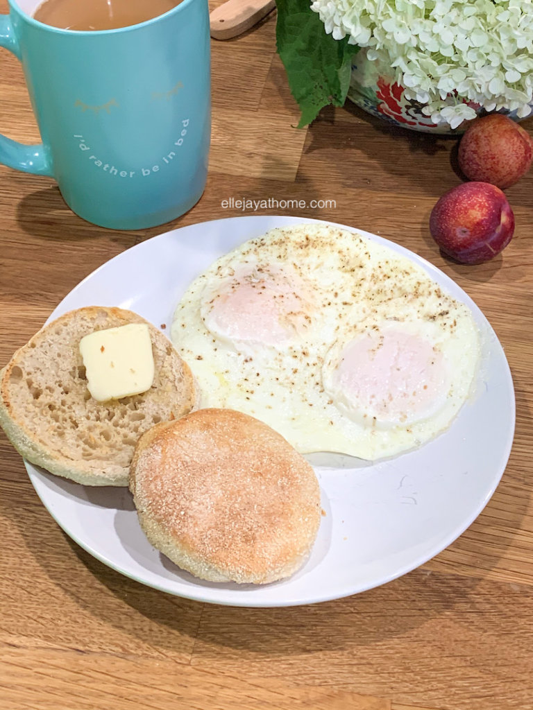 English muffin with a pat of butter beside two eggs and coffee for a complete breakfast.