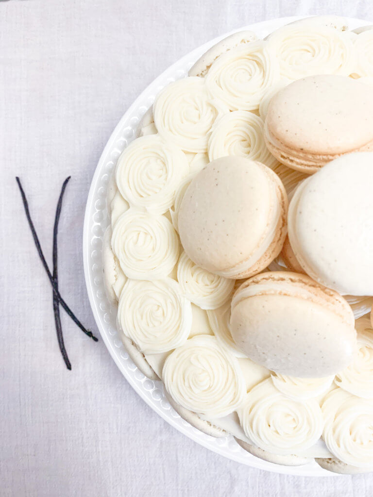 vanilla bean cake with swirls of cream cheese frosting and a pile of vanilla bean macarons on top