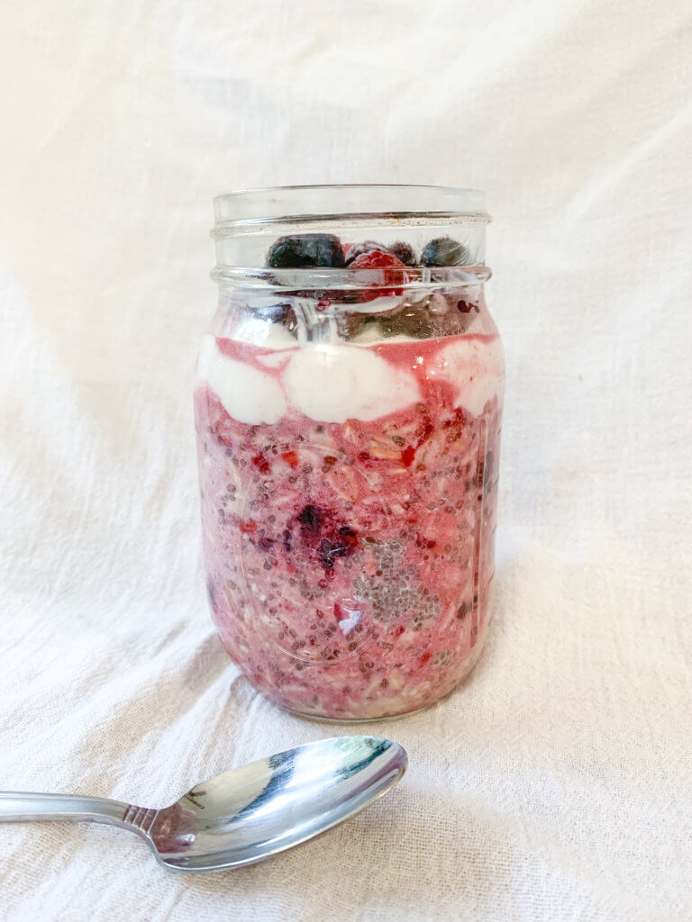 Berry Chia Overnight Oats in a jar, mixed up and topped with greek yogurt and frozen berries