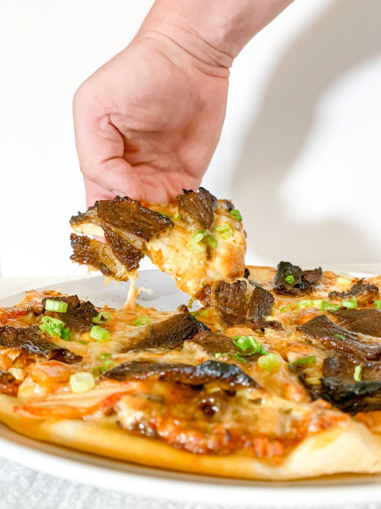 cheese pull on a slice of kimchi and bulgogi pizza