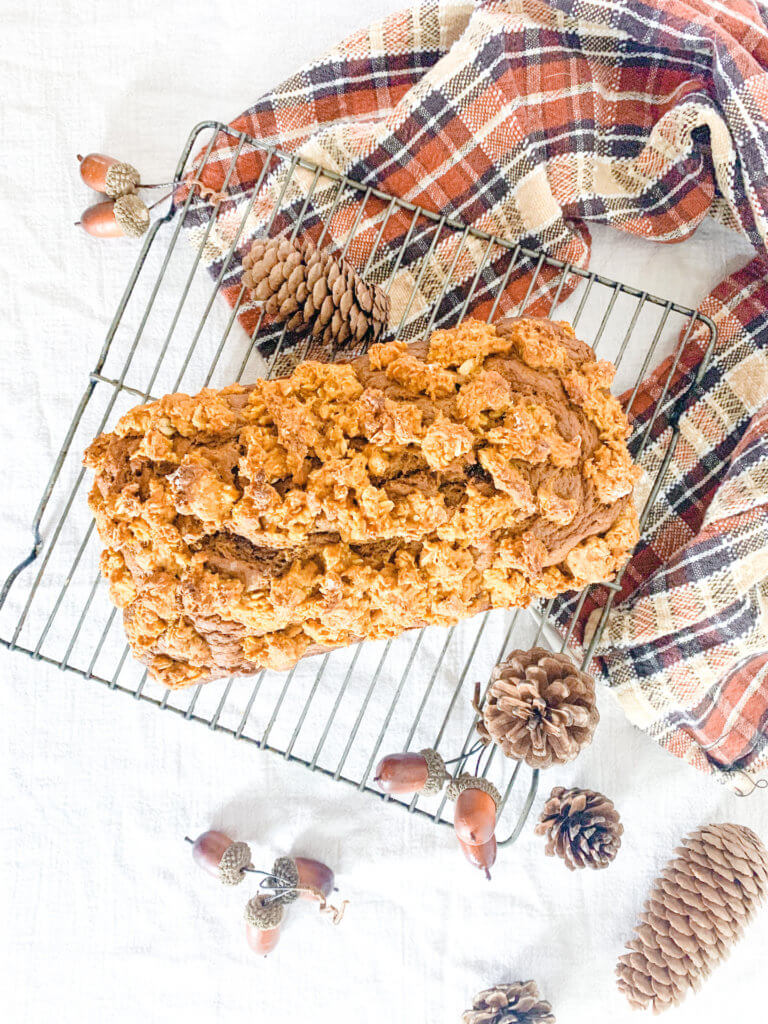 overhead shot of pumpkin streusel loaf cake surrounded by an orange and brown plaid towel and pine cones and acorns
