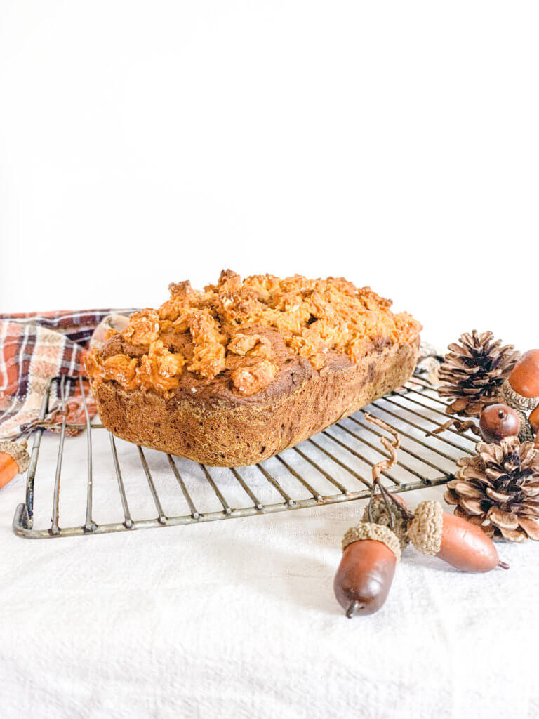 Pumpkin streusel loaf cake on a wire cooling rack with pinecones and acorns and a fall plaid dishtowel in the background