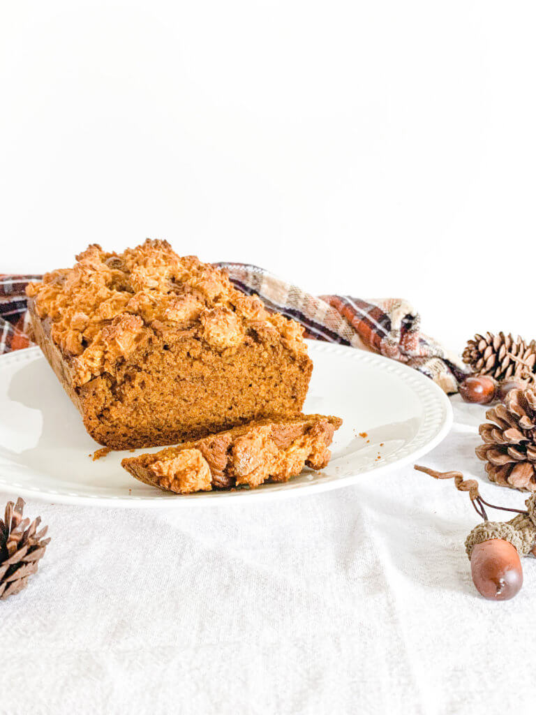 Front view of pumpkin streusel loaf cake with orange and brown plaid dishtowel in the background and pinecones and acorns in the mid and foreground.