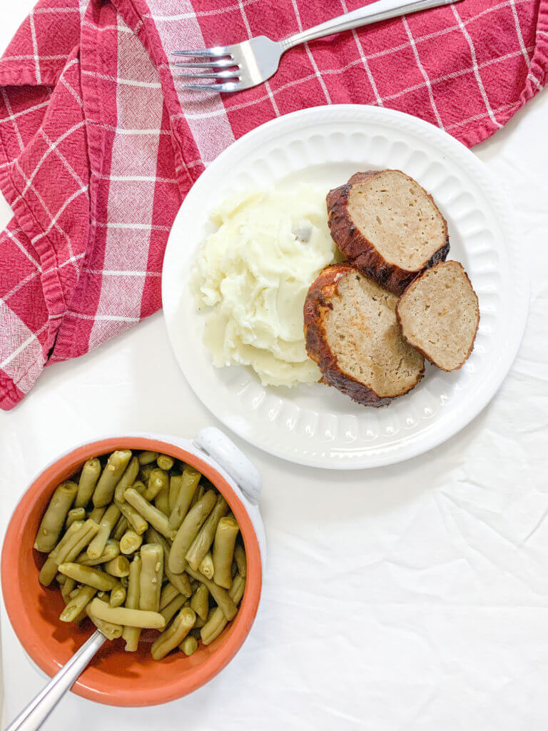 A heaping pile of mashed potatoes with three slices of turkey meatloaf laying against it. 