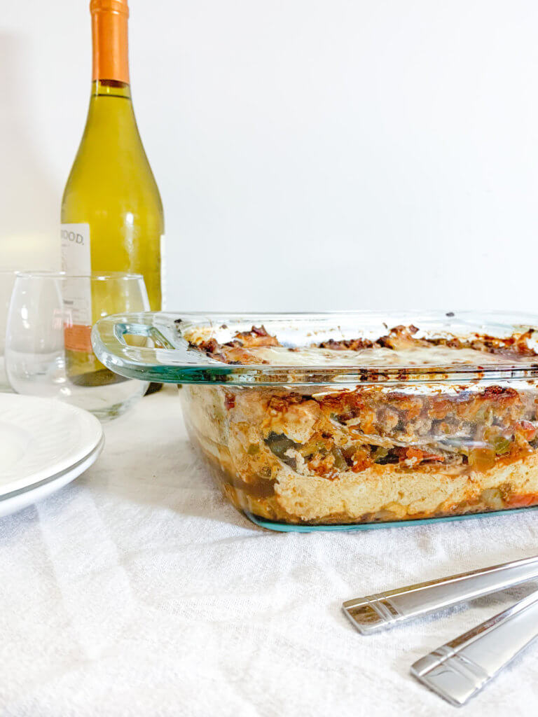 Sideview of eggplant tofu lasagna in a casserole next to a bottle of wine