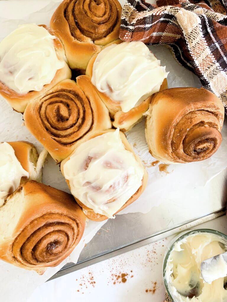 Overhead of cinnamon rolls, some on their side, some frosting, and a plaid towel around them