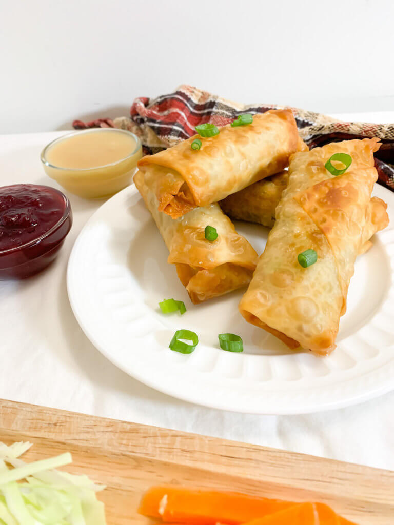 front image of pile of thanksgiving leftover egg rolls on a plate with two sides of dipping sauces