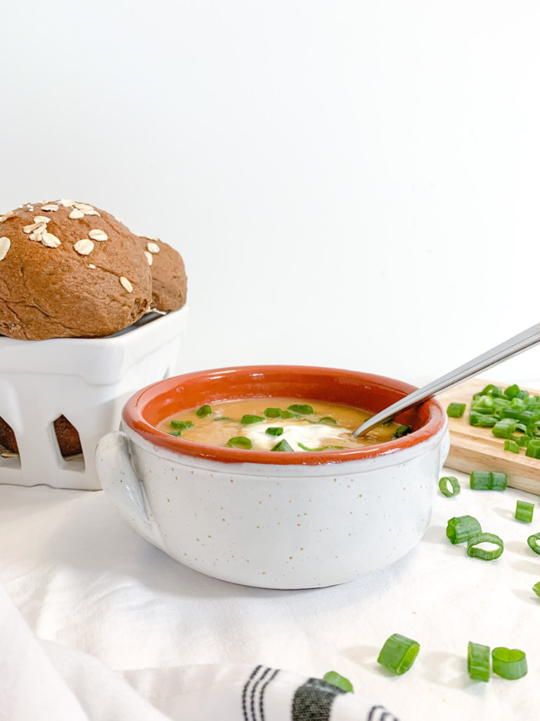Bowl of instant pot loaded potato soup and a basket of brown bread rolls