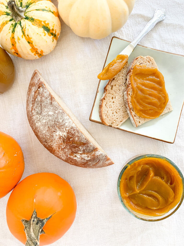 Overhead of pumpkin butter spread on a rustic loaf with pumpkins surrounding