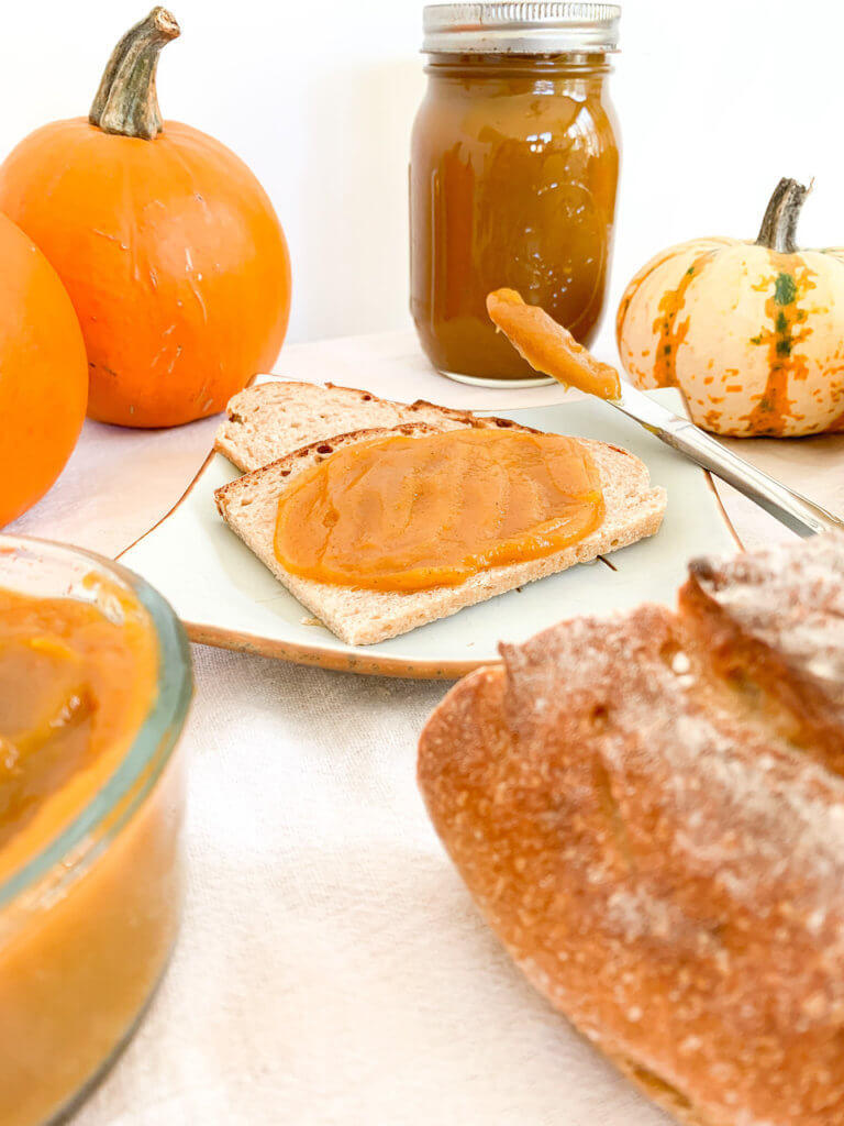 Forward shot of pumpkin butter on toast with a jar of butter in the back, and pumpkins around