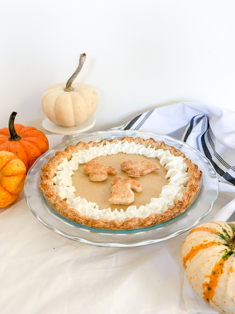 angled shot of white pumpkin pie with decorative pumpkins surrounding