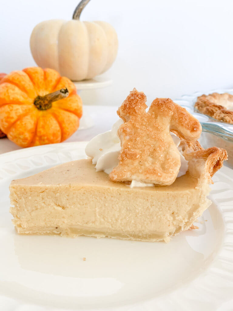 Slice of white pumpkin pie with a pie crust squirrel on top and decorative pumpkins in the background.