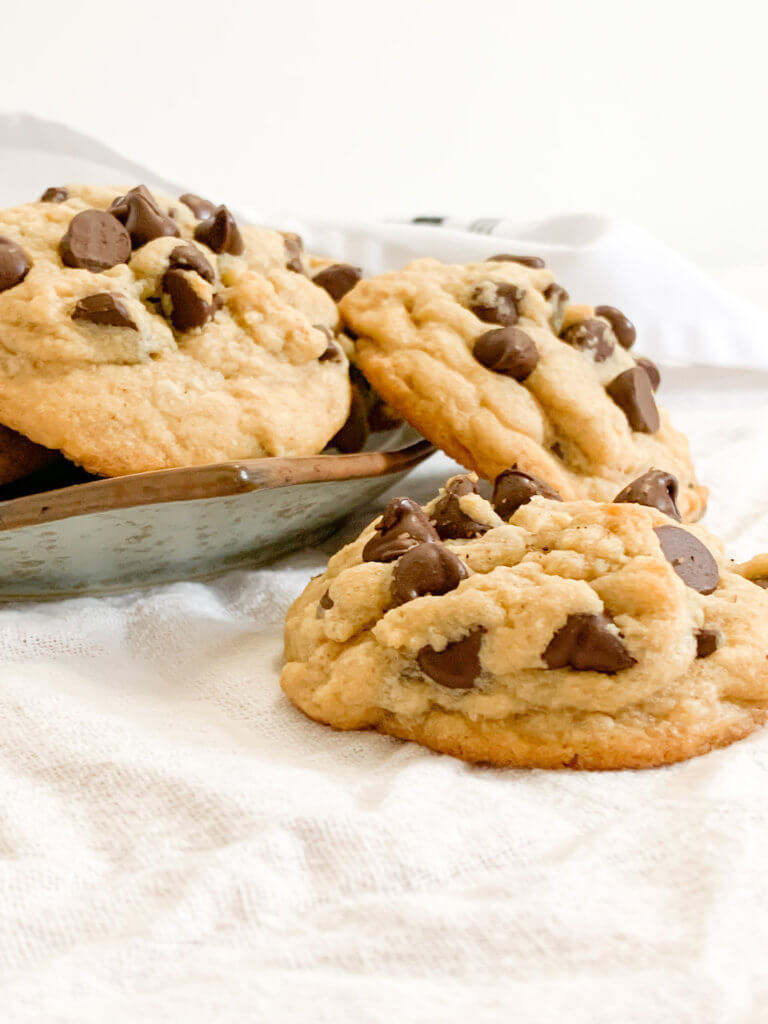 chocolate chip cookies falling off a plate on a white tablecloth against a white wall