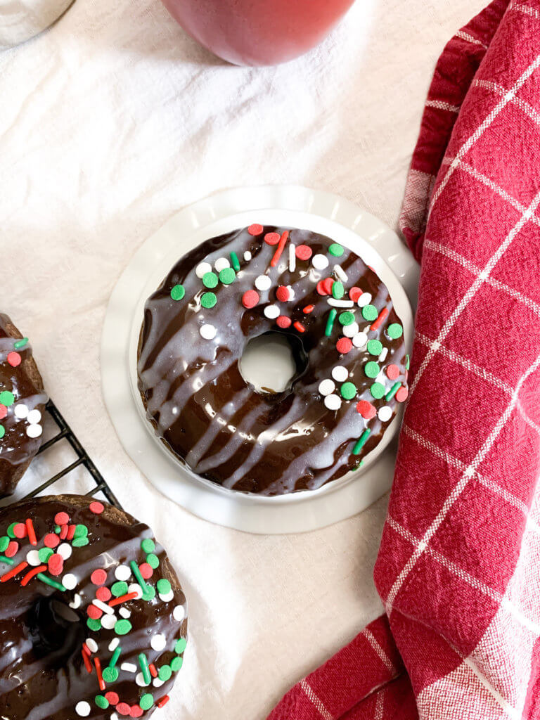 peppermint mocha donut on a ruffled pedestal next to a cooling rack of donuts and a towel