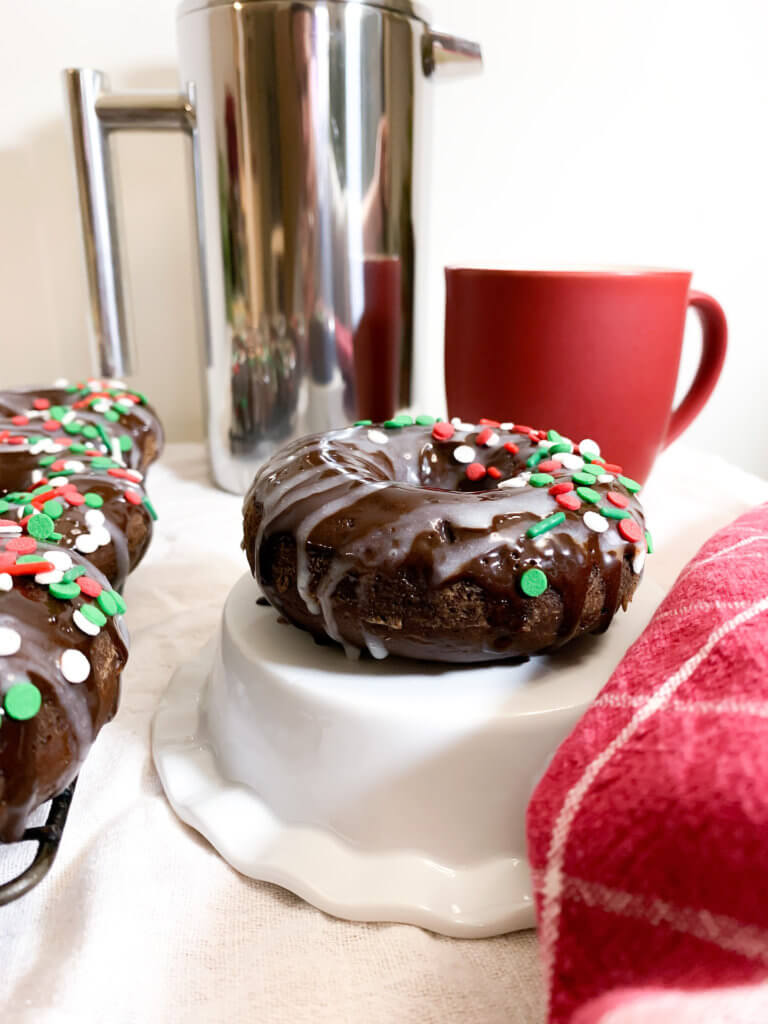 peppermint mocha donut on a ruffled pedestal next to a cooling rack of donuts and a towel from the front