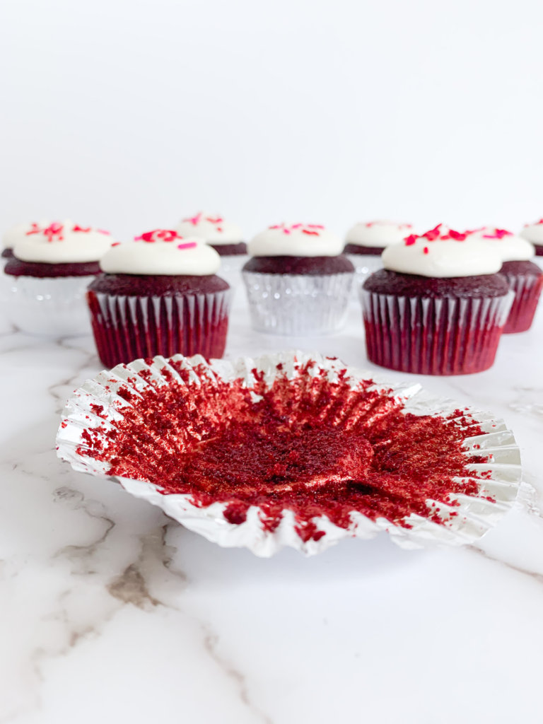 empty cupcake liner in front of red velvet cupcakes
