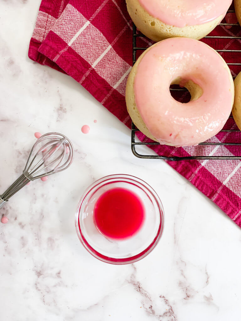 Blood orange juice in a cup  next to a whisk and a blood orange vanilla donut