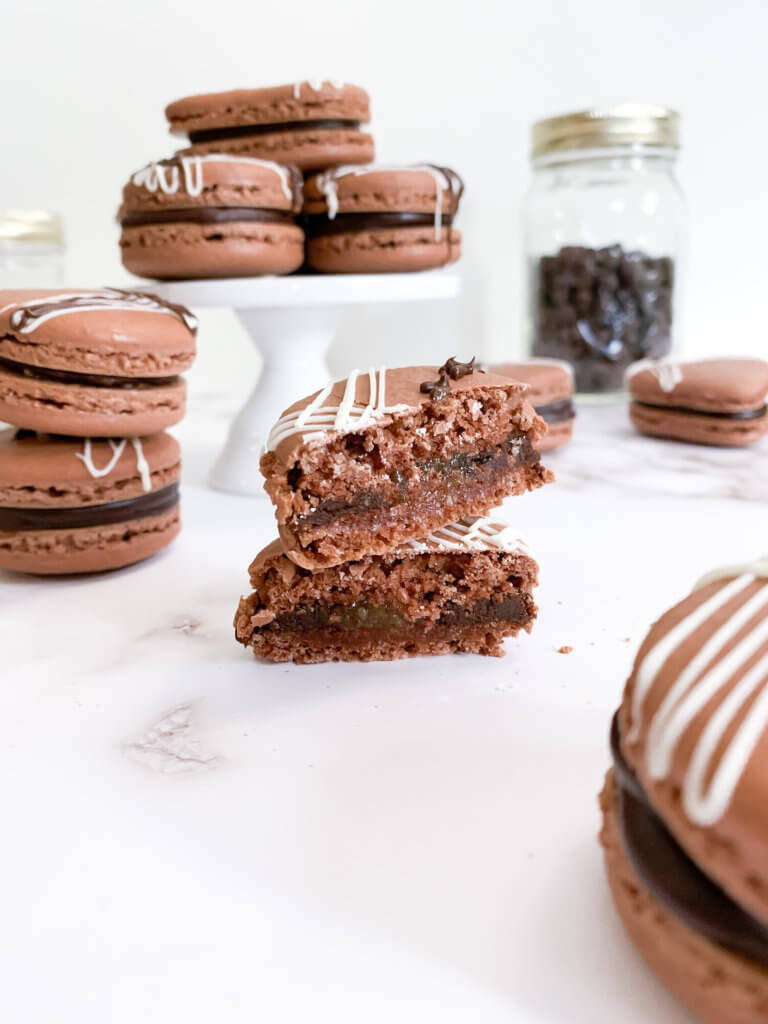 Cut open chocolate almond macaron on a white counter with more stacked around.
