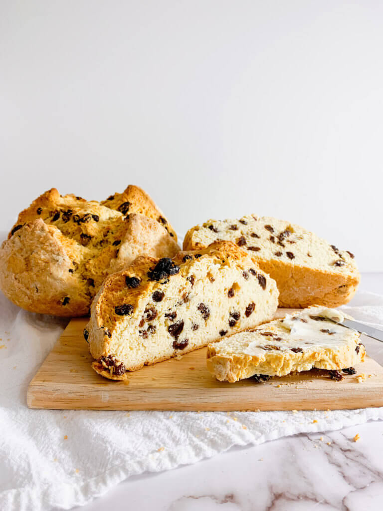 Irish soda bread sliced with butter in front of cut open loaf and whole loaf.