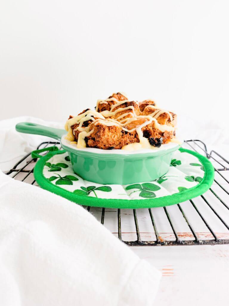 irish soda bread pudding in a green enamel pan on a clover potholder on a wire cooling rack