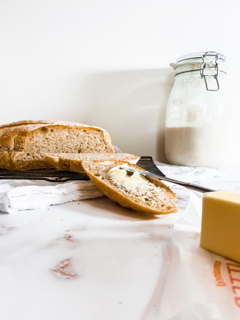 Slice of sourdough bread with butter being spread on it.