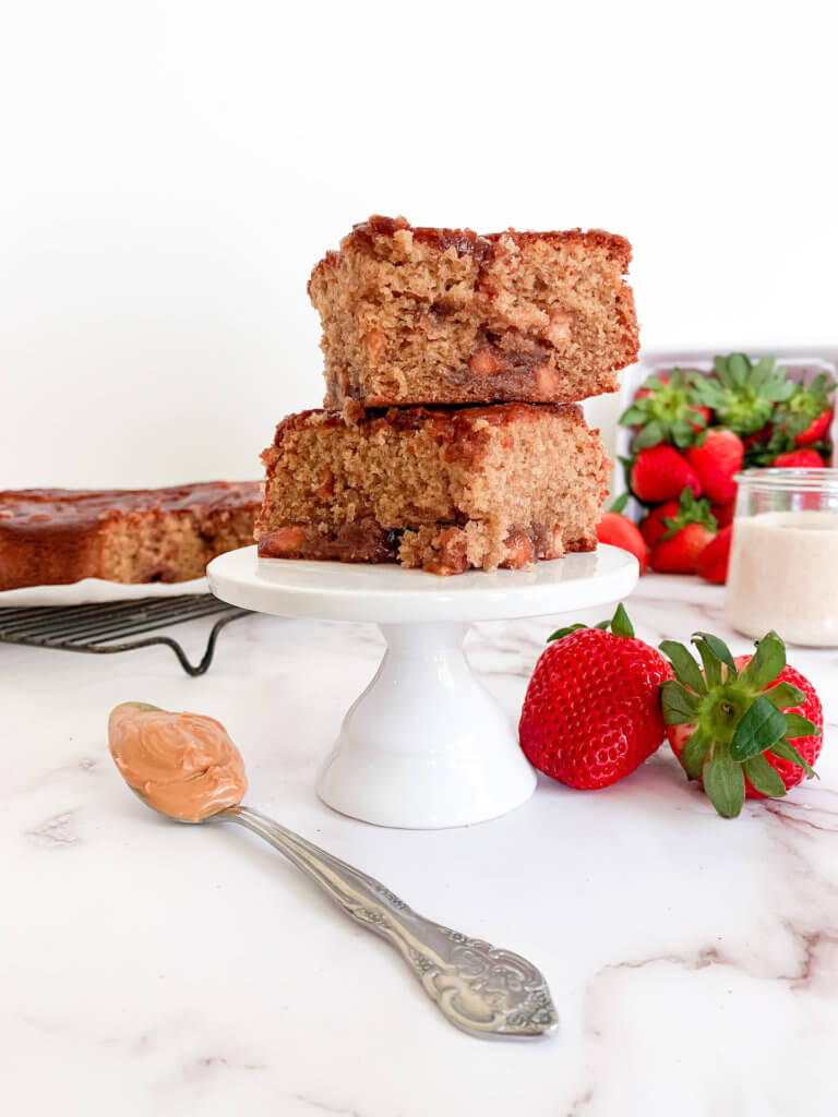 Two sourdough pb&j blondies on a pedestal with a spoonful of peanut butter and strawberries