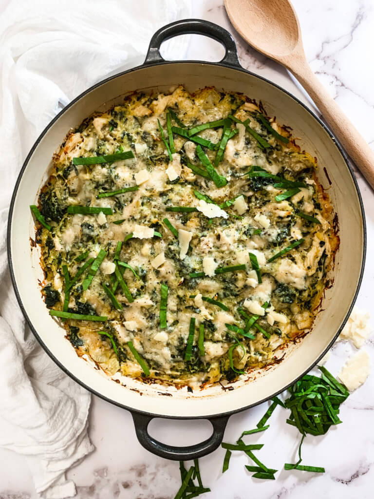 Low Carb Spinach Artichoke Casserole in a enamel skillet on a white marble counter