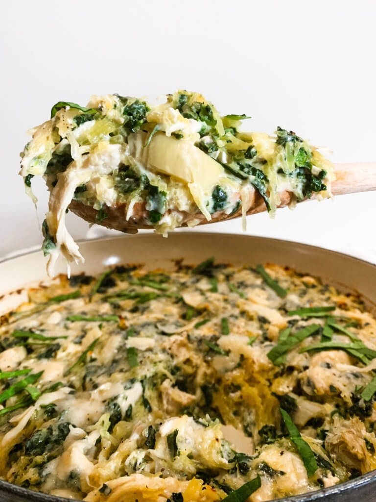 Wooden Spoon holding a serving of spinach artichoke casserole