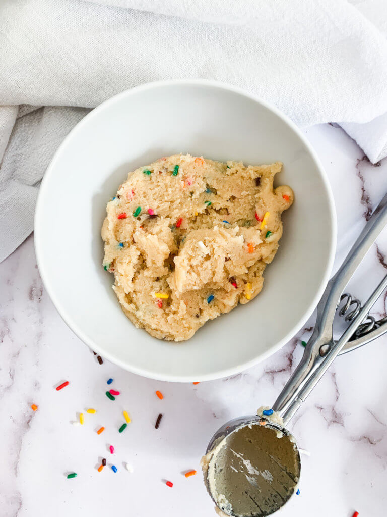 sprinkle cookie dough in a white bowl with a cookie scoop