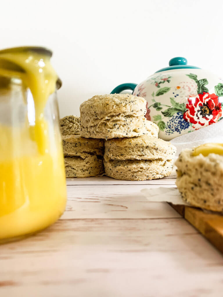 Focus on a pile of scones behind a pot of dripping lemon curd.