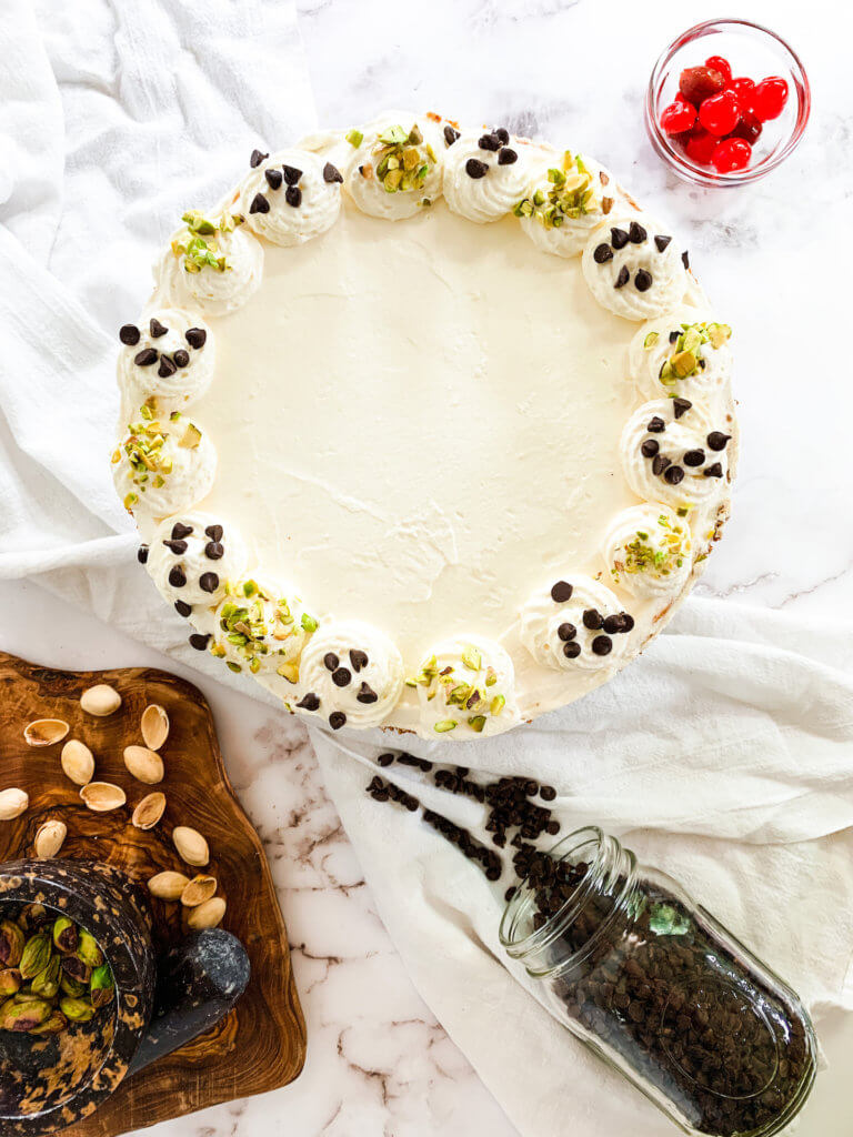 Overhead view of a cannoli cheesecake with pistachios and chocolate chips on the whipped cream decorations