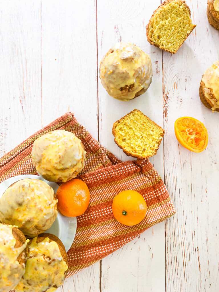 Overhead shot of glazed clementine muffins on a whitewashed wood surface with an orange striped towel and clementines