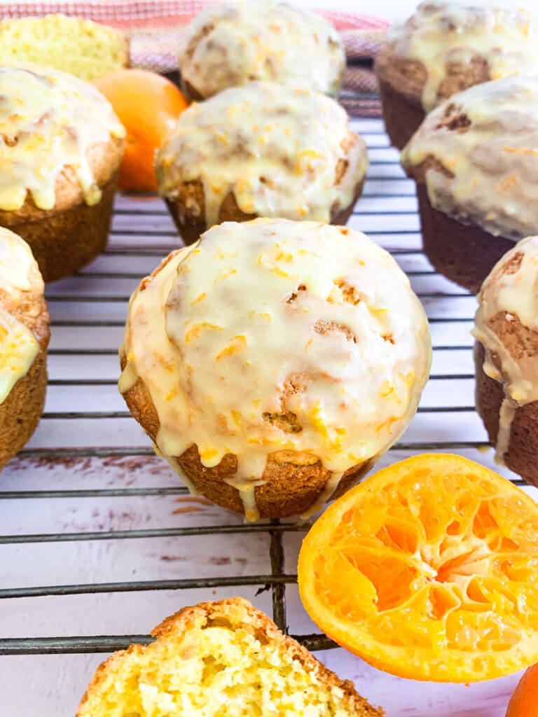 Close up of glazed clementine muffins on a cooling rack with a squeezed half clementine