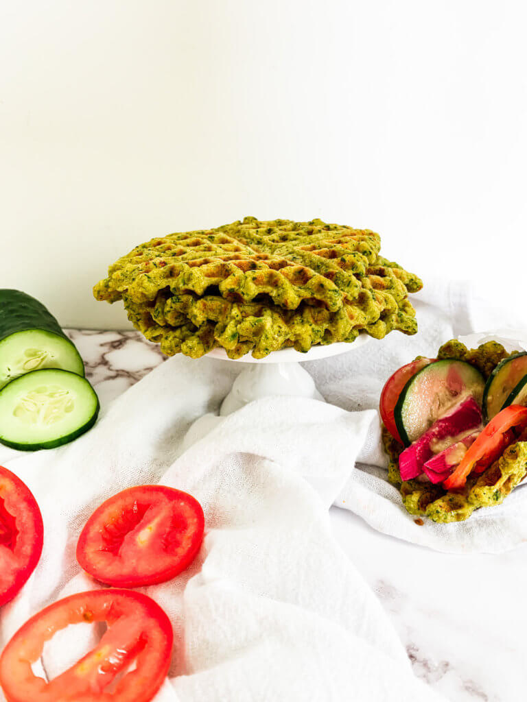 stack of falafel waffles on a pedestal with cucumber and tomato and a loaded waffle gyro