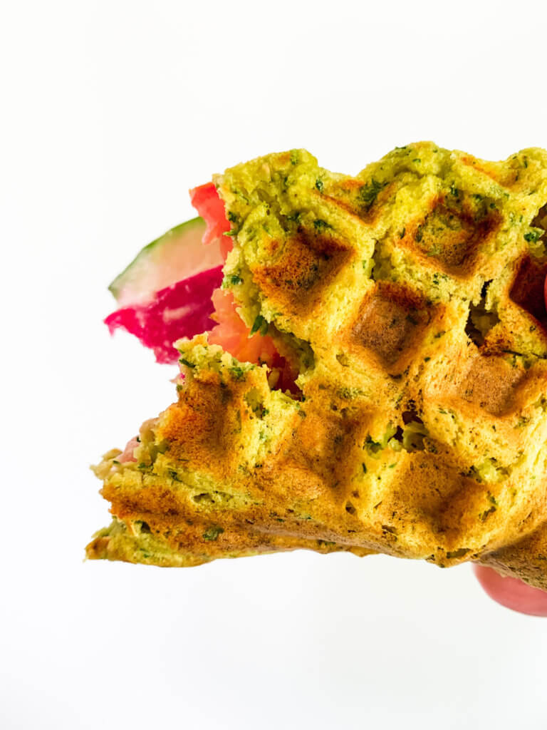 Closeup of a falafel waffle sandwich with a bite taken out of it.