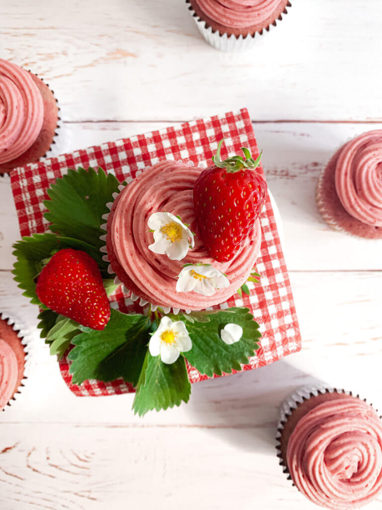 The best strawberry cupcakes ever on a red gingham napkin with strawberry leaves and blossoms