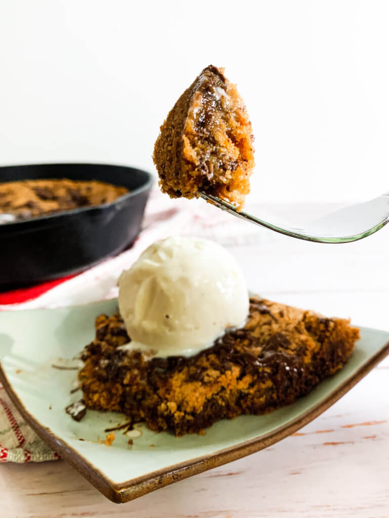 A bite of chocolate chunk cookie on a fork in front of a skillet cookie