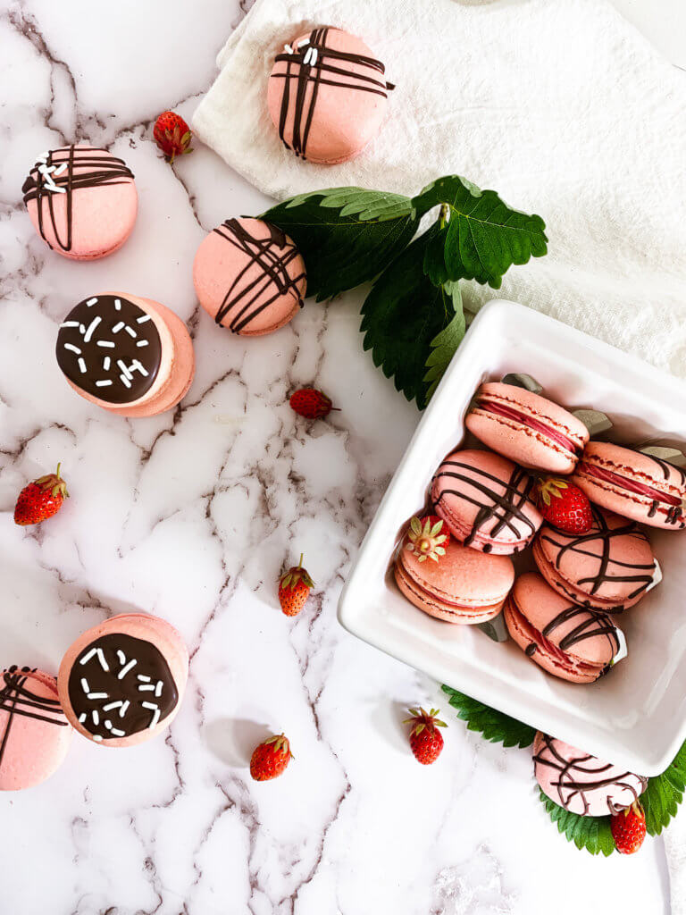 Strawberry cheesecake macarons in a berry basket with little strawberries on a white counter