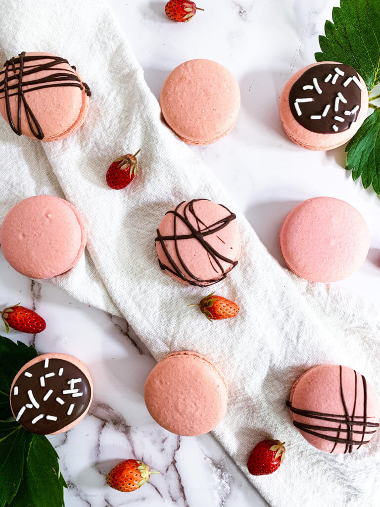 9 strawberry cheesecake macarons in varying degrees of chocolate drizzle