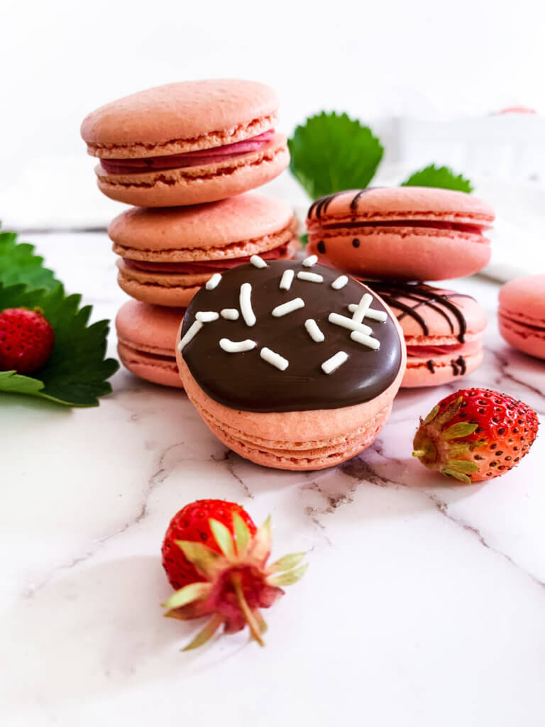 strawberry cheesecake macarons stacked up with berry leaves in the background and strawberries in front