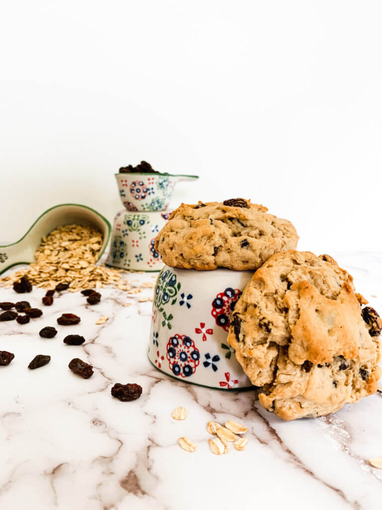 Oats and raisins in hand painted measuring cups with two oatmeal raisin cookies