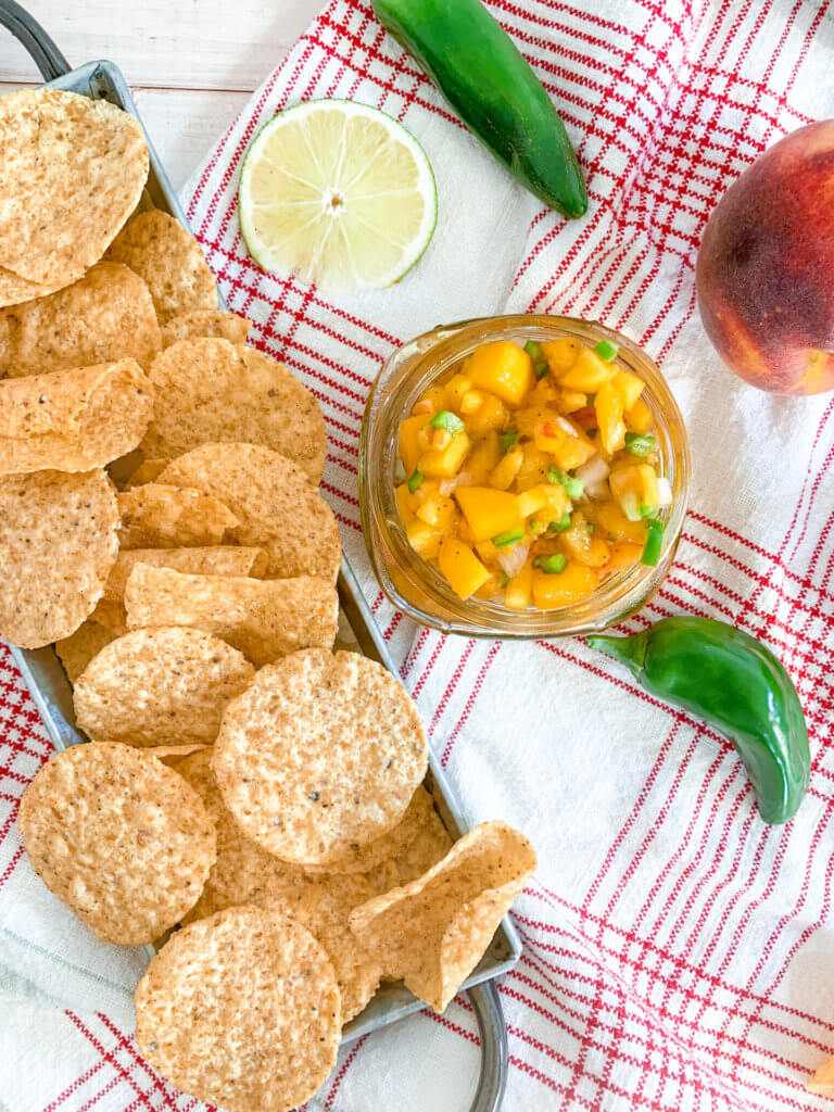 spicy peach salsa served with tortilla chips on a white and red plaid dish towel