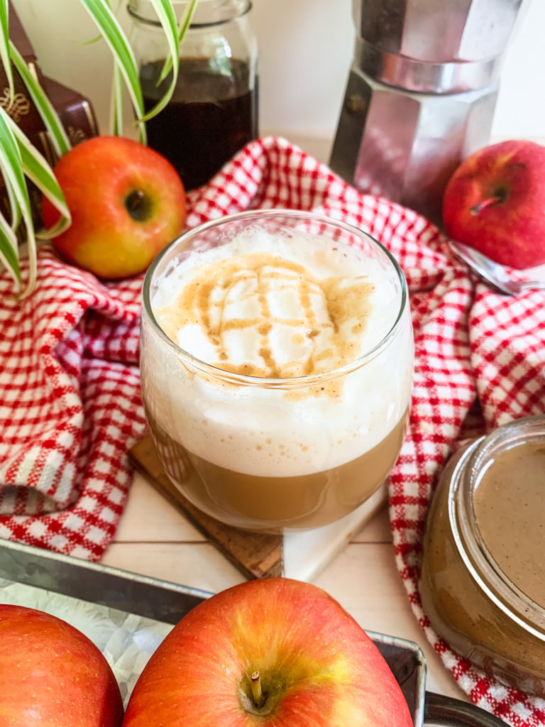 apples and apple spice caramel in a jar surround a glass of apple crisp macchiato
