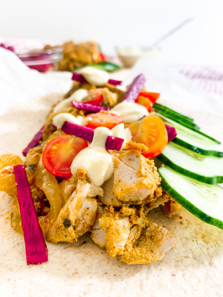 Close up of assembled chicken shawarma wrap with pickled turnips, cucumber, tomato, and garlic sauce