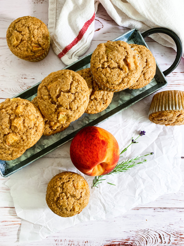 metal tray of peach muffins with a fresh peach and a sprig of lavender on a sheet of crumpled parchment paper