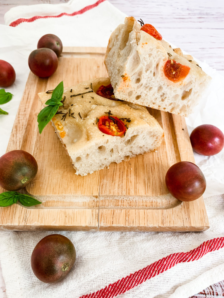 two chunks of focaccia with black cherry tomatoes and fresh basil