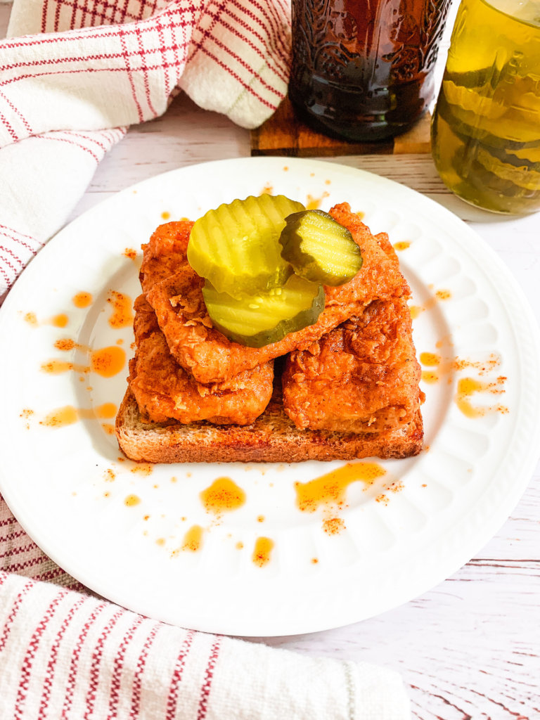 Three slices of vegan Nashville Hot Chik'n on a slice of wheat bread topped with three pickles