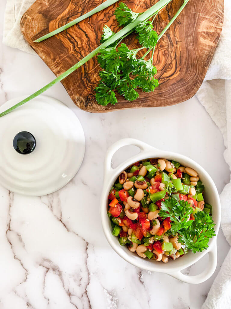 black eyed pea salad in a white crock with parsley and green onion on an olive wood cutting board