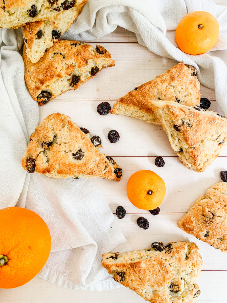 cranberry orange scones on a white wood counter with white linen, oranges, and cranberries